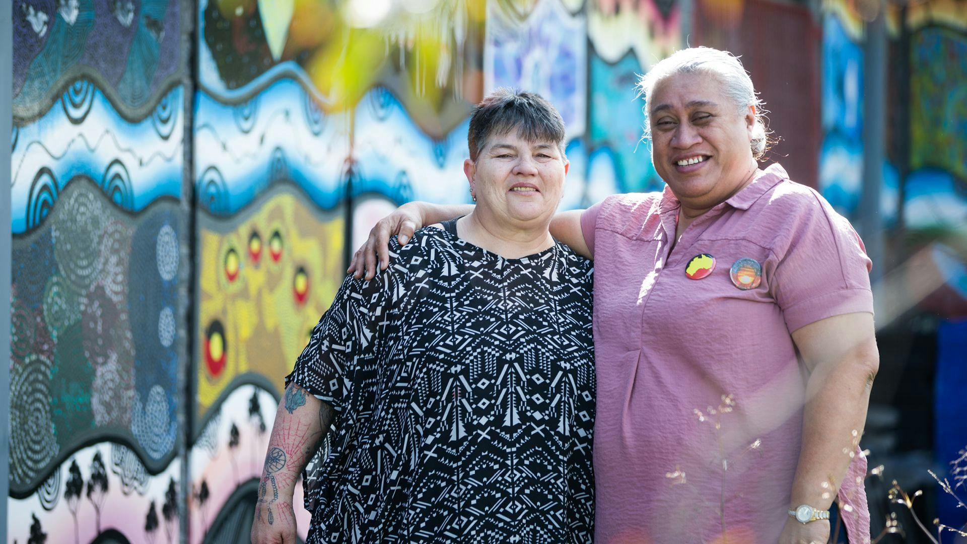 Two women in front of an indigenous mural